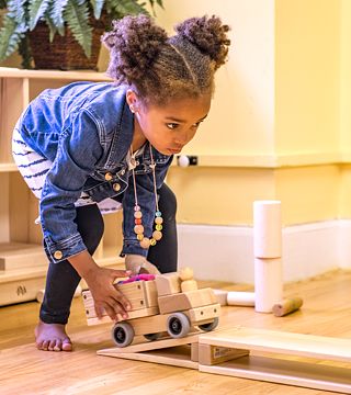 a girl playing with a wooden truck