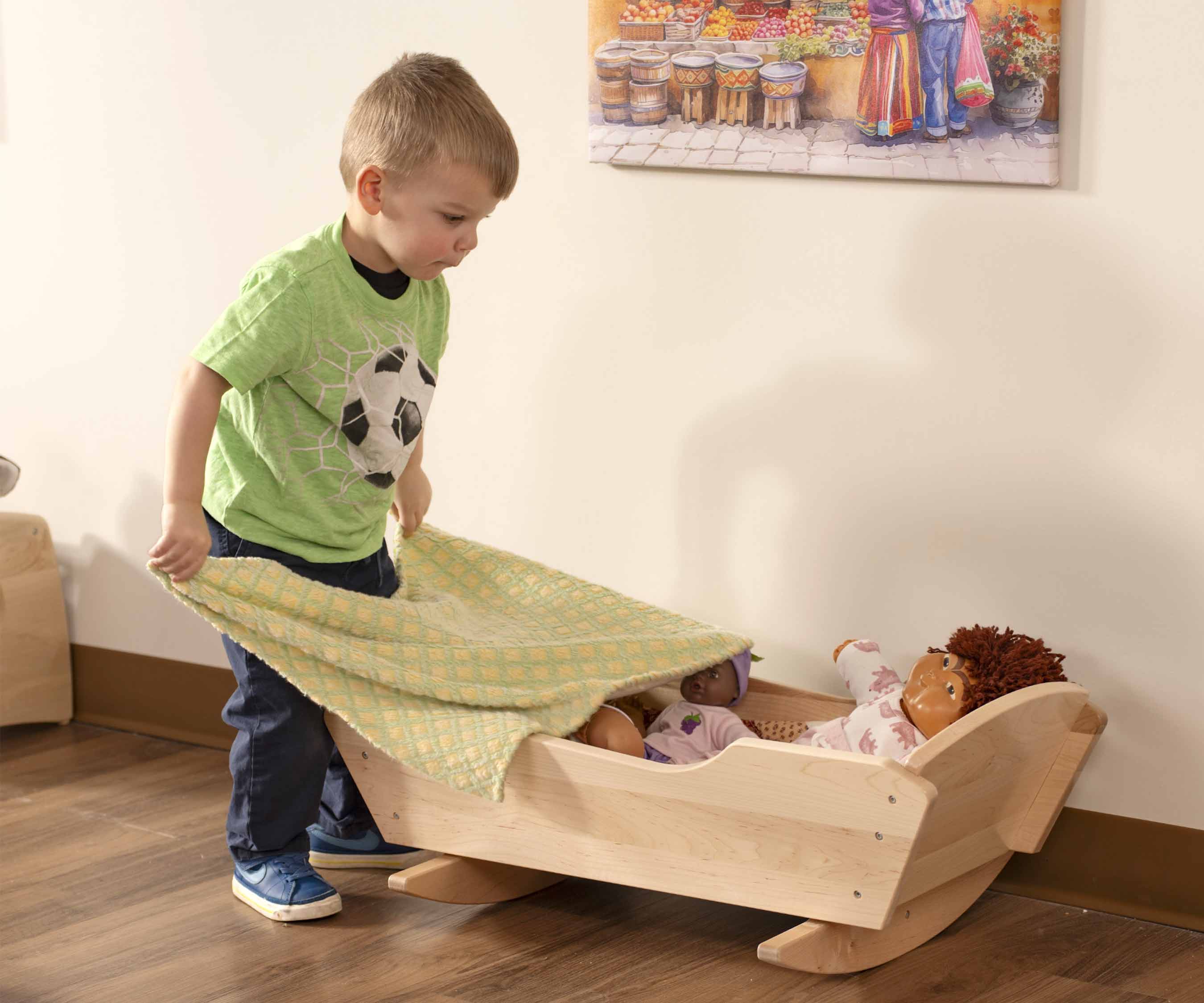 A little boy playing with a dolls cradle