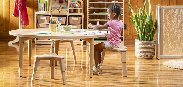 A child sitting on a stool doing a project at a table