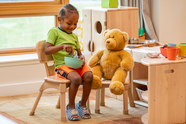 Child and teddy bear seated on Classroom Chairs
