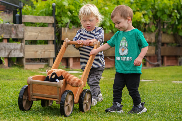Two children pushing a stuffed animal in Outlast Pushcart