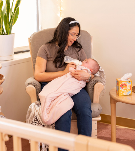 Woman giving baby a bottle in Community Playthings glider