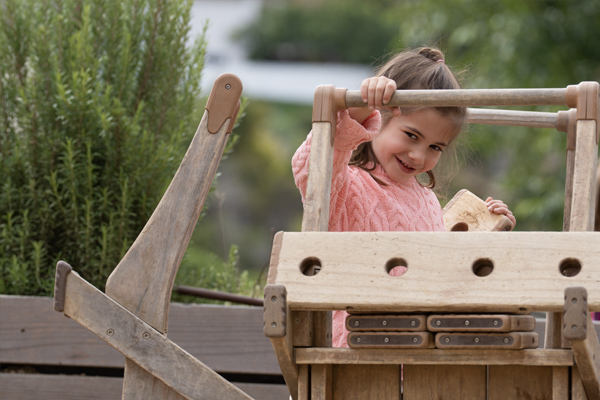 Child looking through handle of Outlast Wheelbarrow that is weathered to a silver gray color.